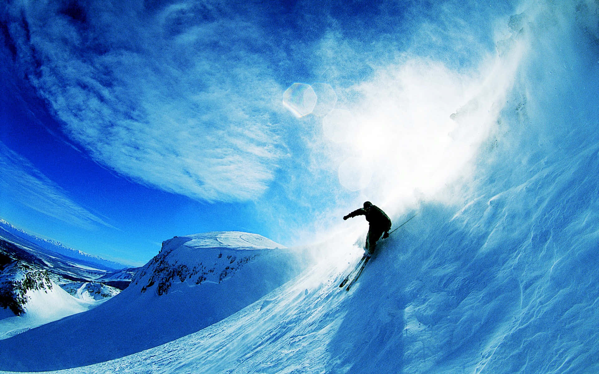 Skiing 桌布 壁紙 — 一名滑雪者正在陡峭的雪坡上轉彎，在充滿活力的藍天下揚起一陣粉雪。
