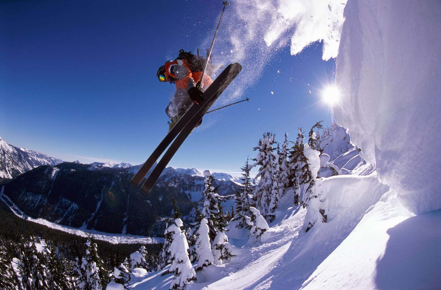 Skiing 桌布 壁紙 — 一名滑雪運動員在冰崖後方陽光照耀的積雪山坡上方，於清爽的冬日空氣中翱翔。