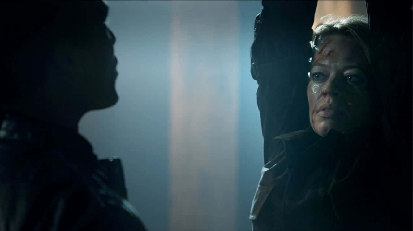 Mortal Kombat Legacy 桌布 壁紙 — 一名滿臉鮮血的女子懸掛在昏暗燈光下，一個陰影人物在緊張的對峙中與她對抗。
