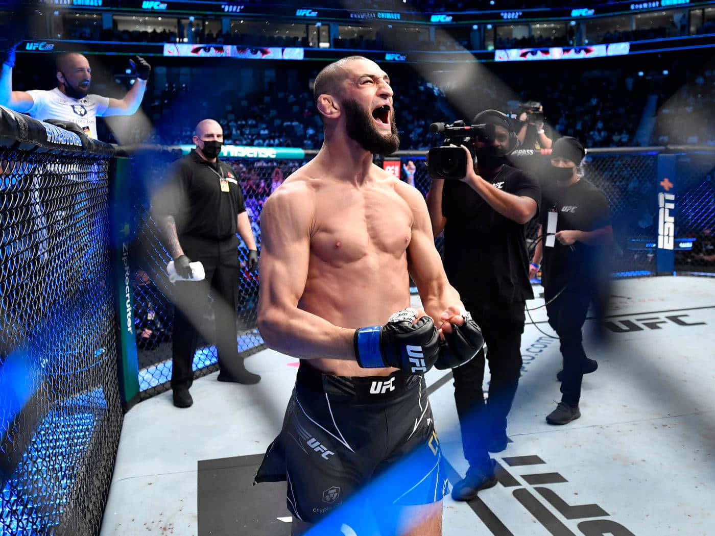 UFC 桌布 壁紙 — 一名獲勝的UFC拳手在八角籠內咆哮勝利，背景是明亮的場館燈光和歡呼的人群。