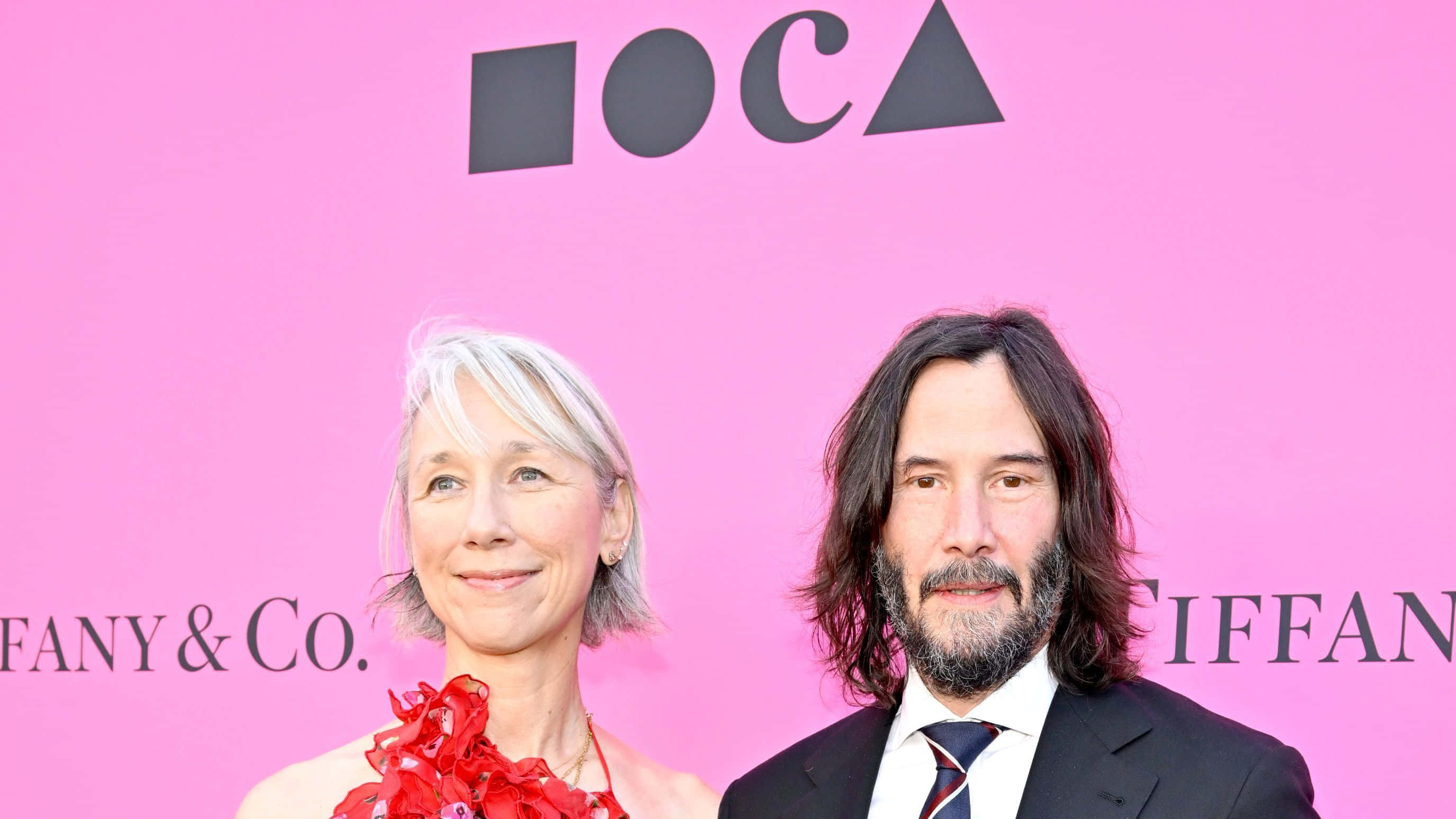 Keanu Reeves 桌布 壁紙 — 一名男子和一名女子在帶有Tiffany & Co.品牌的鮮豔粉紅色背景前一起擺姿勢。