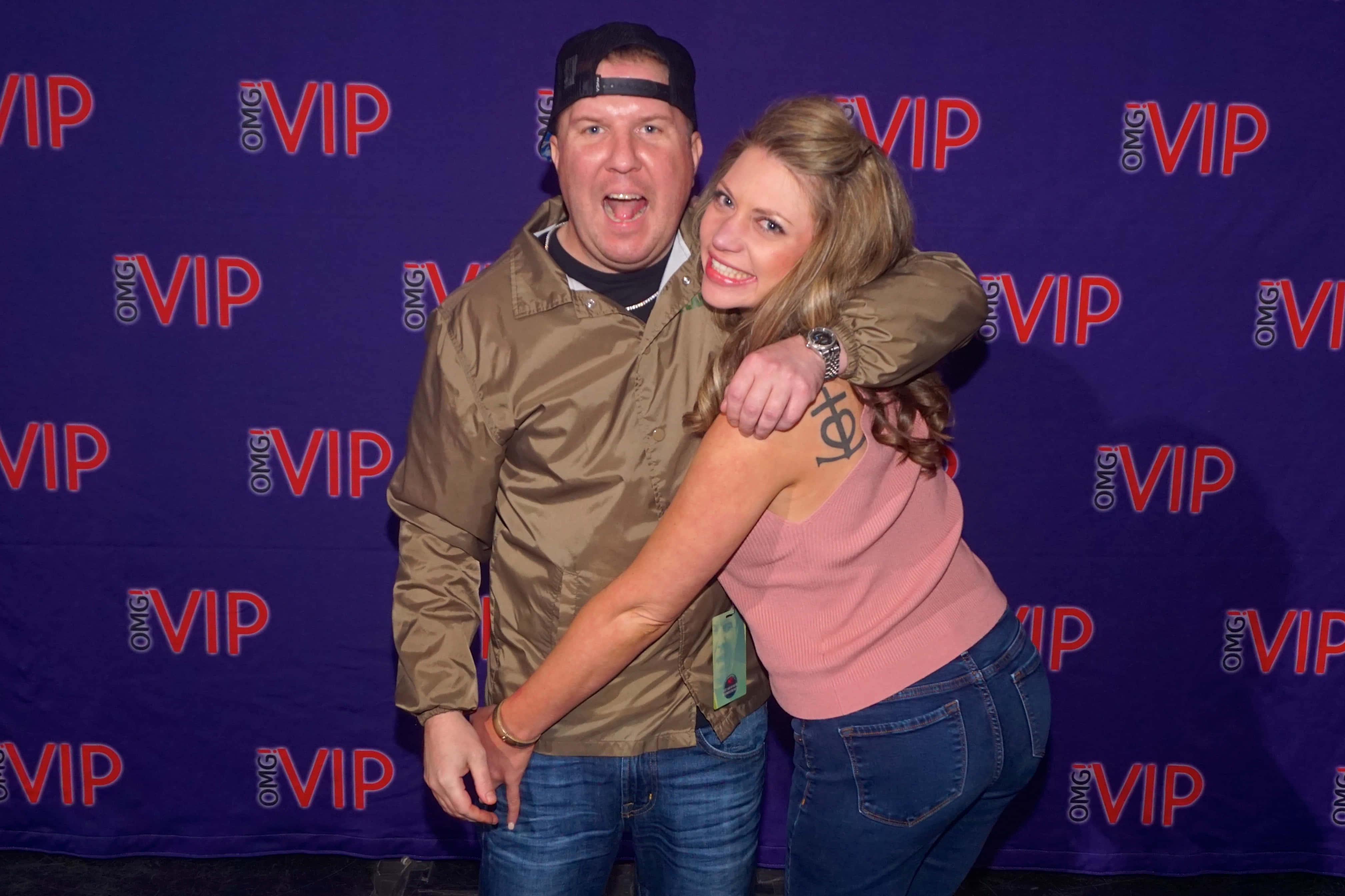 Nick Swardson 桌布 壁紙 — 一名男子和女子在帶有紅色標誌的紫色VIP背景前俏皮地擺姿勢。