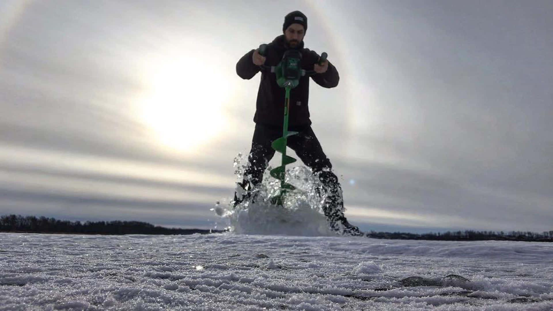 Ice Fishing 桌布 壁紙 — 一名男子在積雪湖上鑽穿冰層，身後有太陽耀斑。