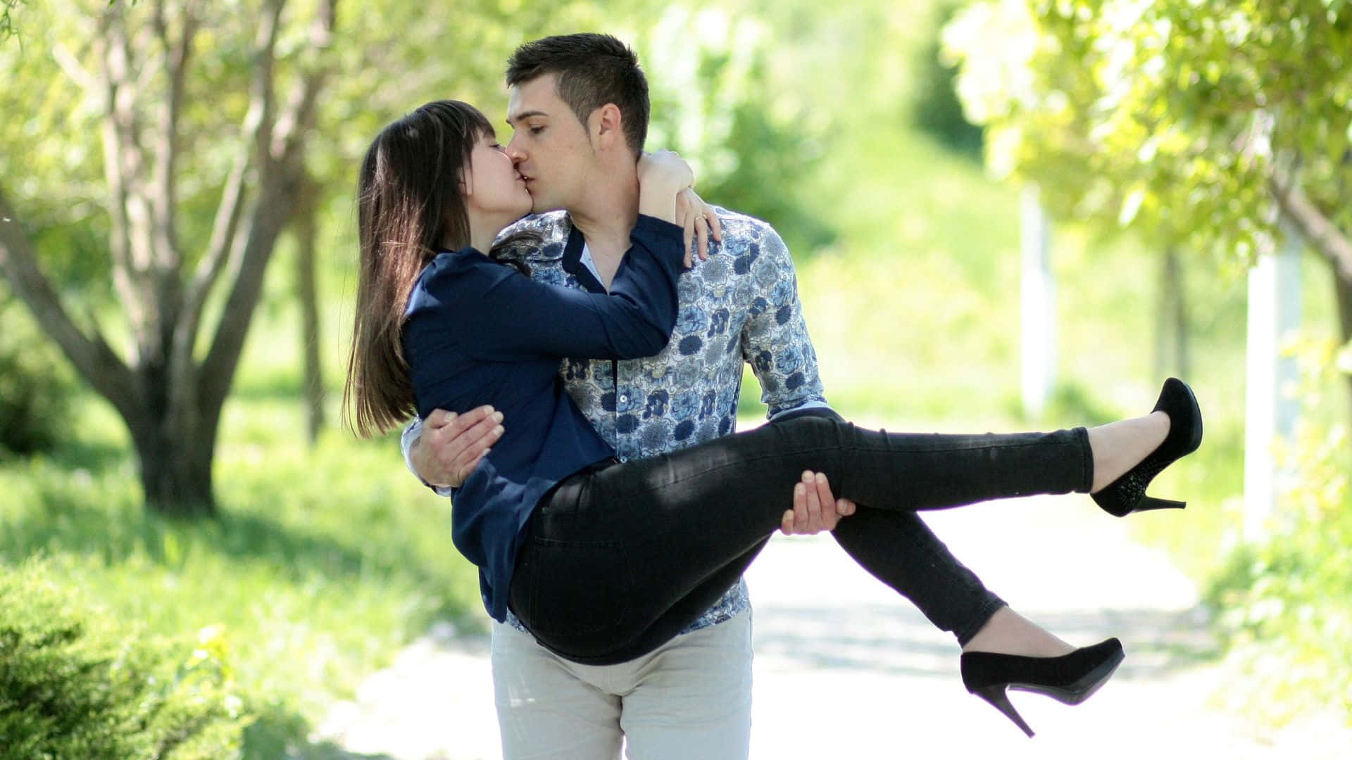 Beautiful Love 桌布 壁紙 — 一名男子在陽光明媚的公園裡，被綠樹和草地環繞，抱起一名女子親吻。