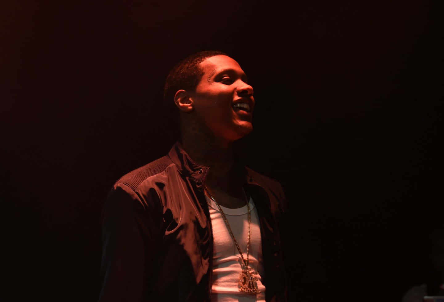 lil durk 桌布 壁紙 — 一名男子在黑暗背景下，於戲劇性的紅色舞台燈光下溫暖地微笑。