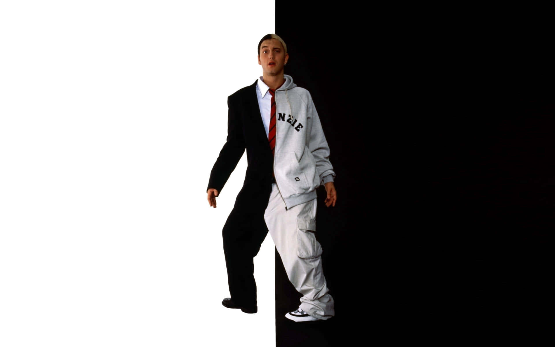 Eminem 桌布 壁紙 — 一名男子從中間分開站立，一邊穿著黑色西裝，另一邊穿著灰色連帽衫，背景為鮮明的白色和黑色。