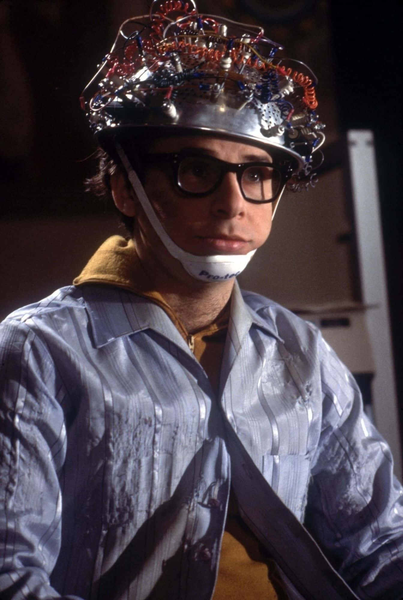 rick moranis 桌布 壁紙 — 一名男子戴著一個佈滿電線和管子的頭盔，嘴上有一個白色封口物，並戴著黑色框眼鏡。