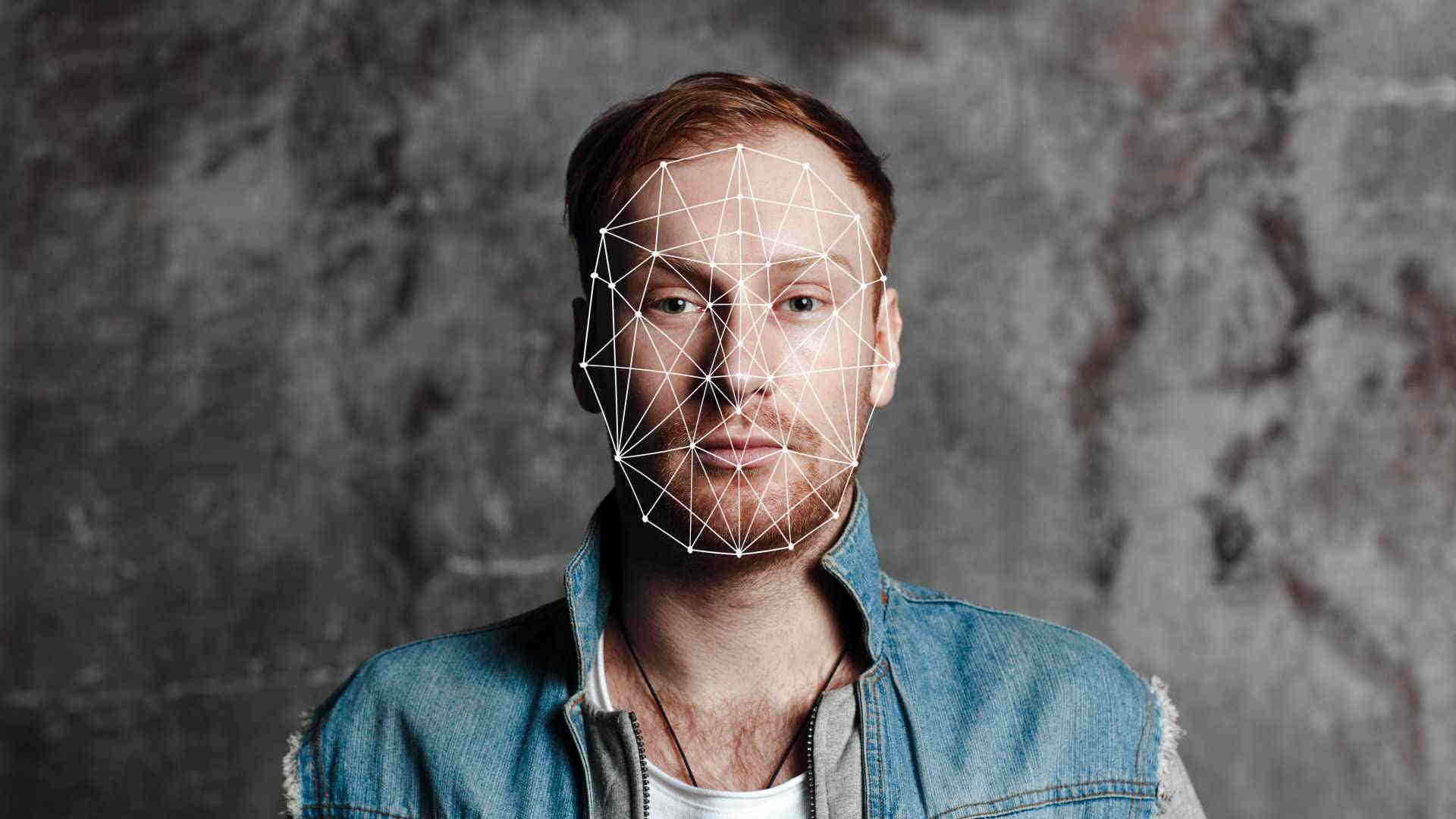Face Recognition 桌布 壁紙 — 一名男子臉上帶有幾何線框疊加效果，背景為有紋理的灰色牆壁。