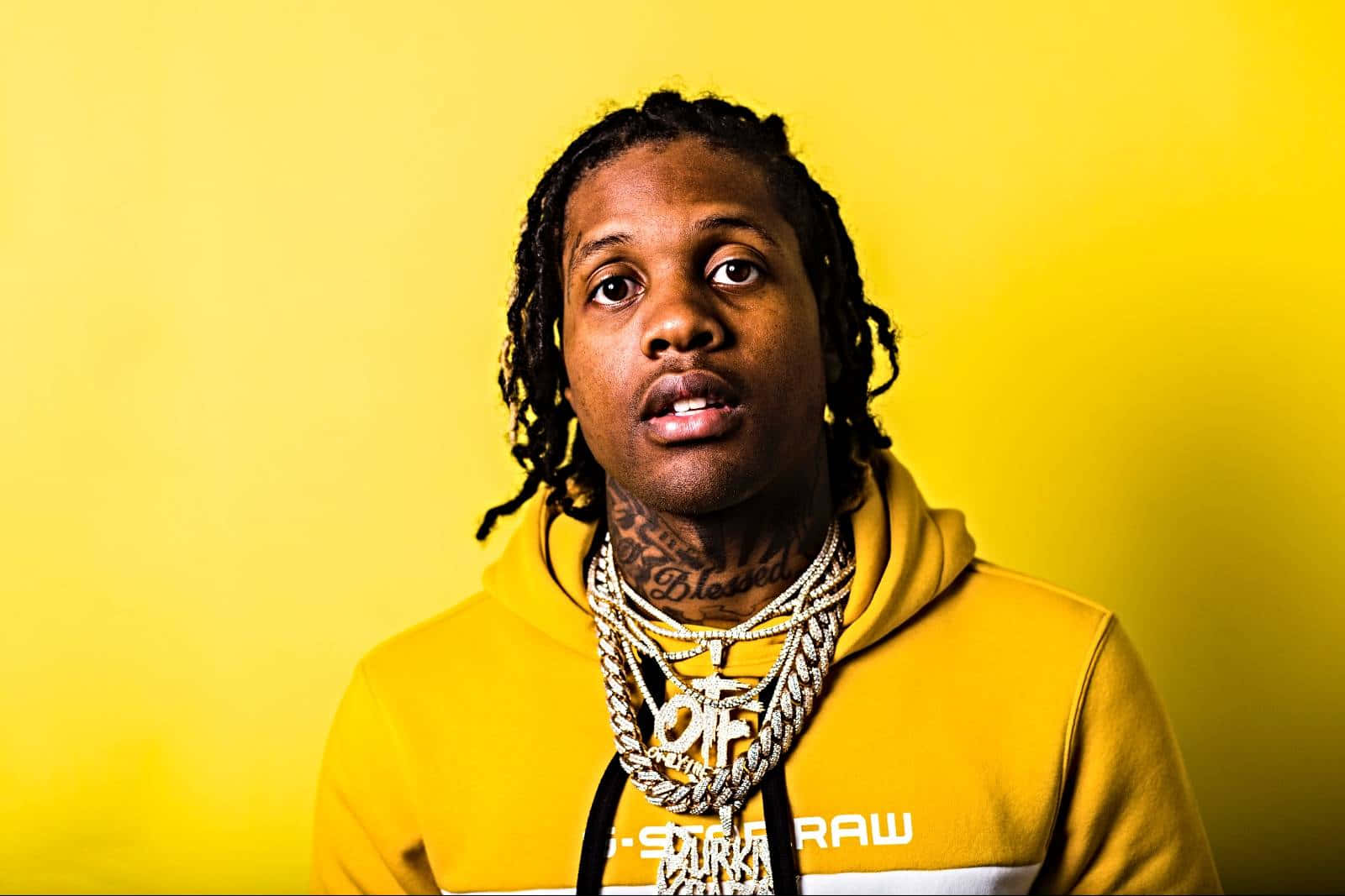 lil durk 桌布 壁紙 — 一名留著辮子頭和紋身的男子，穿著黃色連帽衫和層疊的金鏈，背景是純黃色。