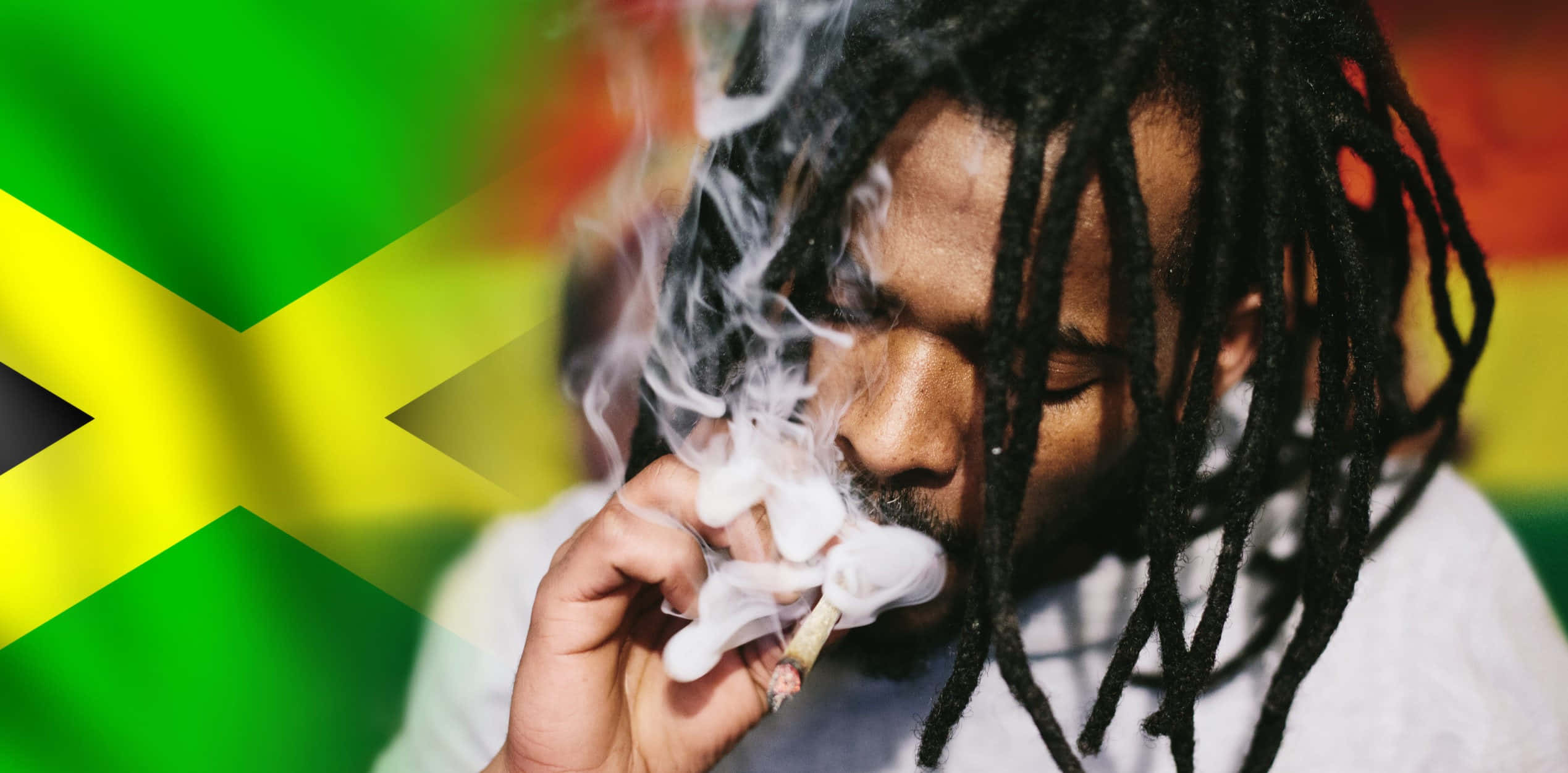 Jamaica 桌布 壁紙 — 一名留著辮子頭的男人，在充滿活力的牙買加國旗背景下，手持大麻煙並呼出煙霧。