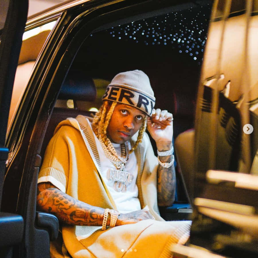 lil durk 桌布 壁紙 — 一名留著辮子頭髮、有紋身的男子，戴著冷帽和金鏈，坐在豪華車內，直視鏡頭。