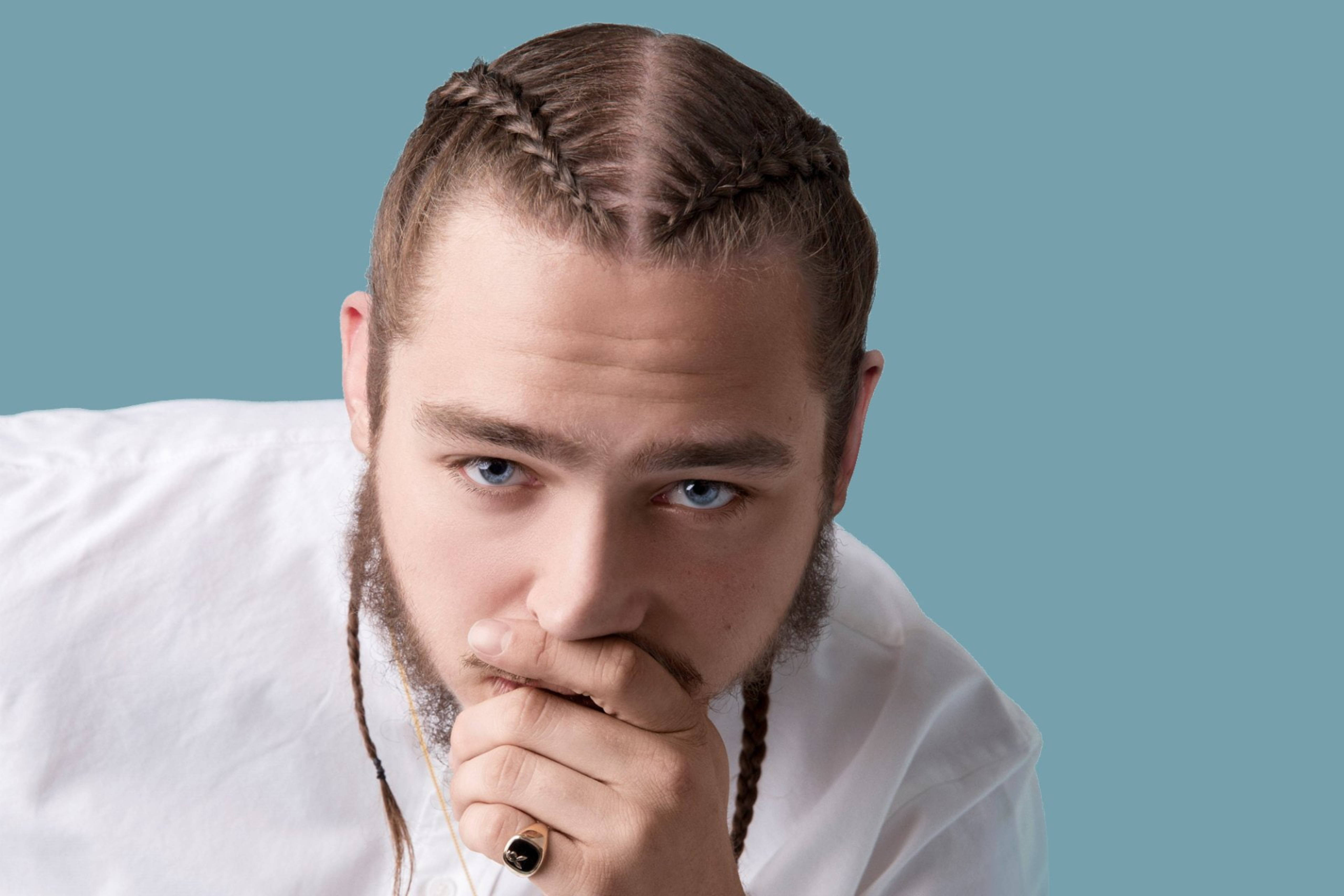 Post Malone The Granada 壁紙 — 一名留著辮子頭髮和鬍鬚的男子，在純青色背景前，將下巴擱在手上，凝視著鏡頭。