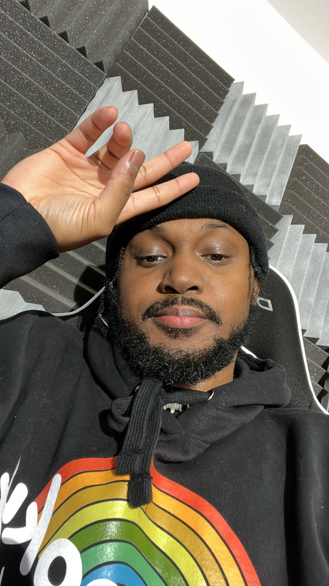Coryxkenshin 桌布 壁紙 — 一名留鬍鬚、戴黑色冷帽的男子在一個設有隔音板的房間內，穿著帶有彩虹圖案的連帽衛衣擺姿勢。