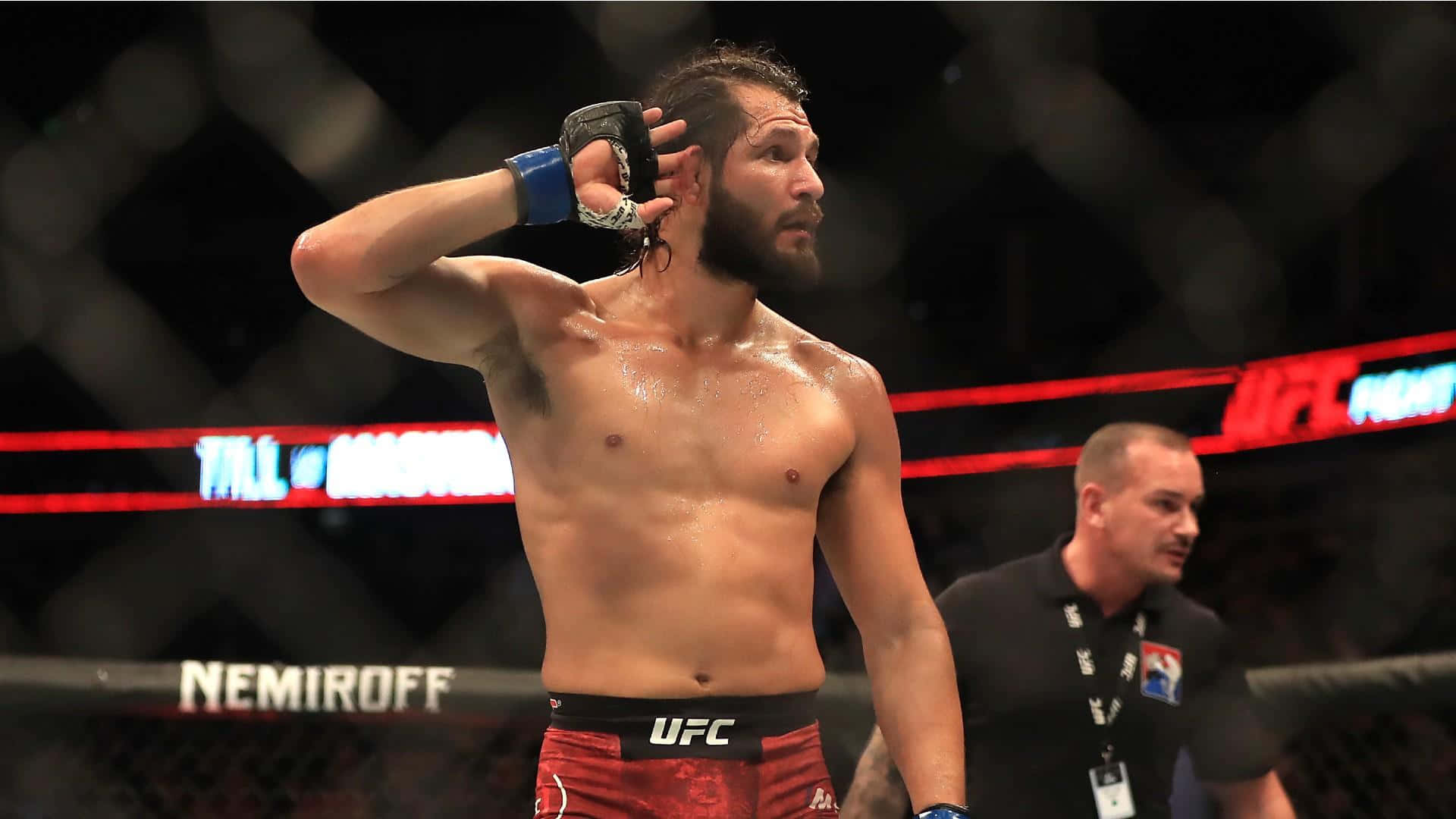 UFC 桌布 壁紙 — 一名留鬍鬚、汗流浹背的 UFC 拳手在明亮的場館燈光下，於八角籠內擦拭額頭上的汗水。