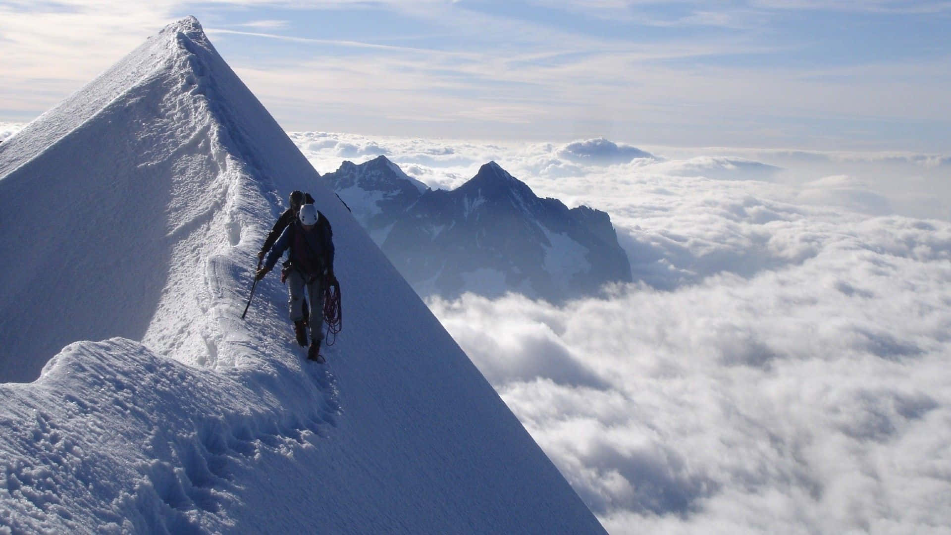 Ice Climbing 桌布 壁紙 — 一名登山者在清澈的藍天下，攀登雲海之上白雪覆蓋的山脊。