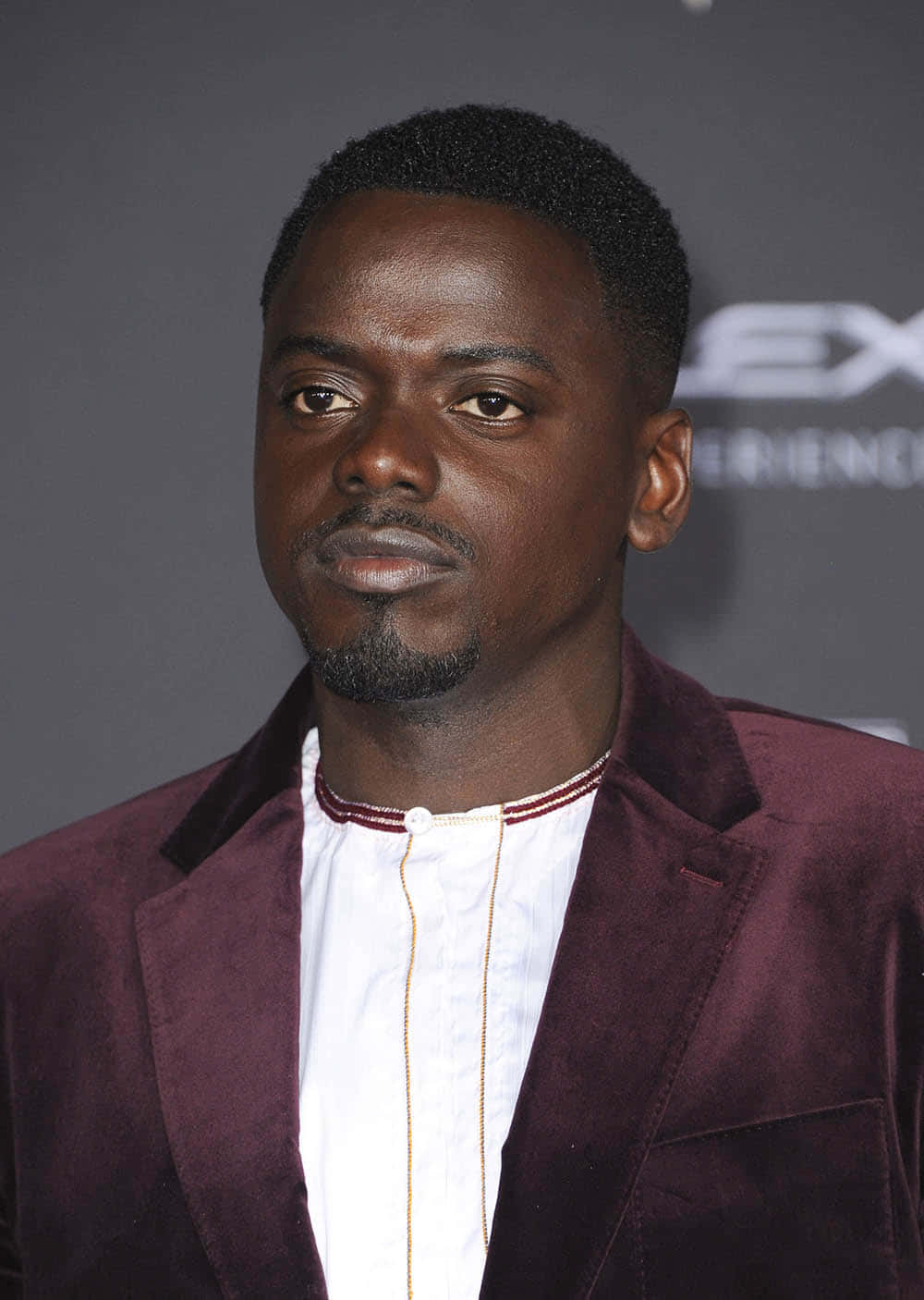 Daniel Kaluuya 桌布 壁紙 — 一名短黑髮、留山羊鬍的男子，在灰色背景前穿著酒紅色天鵝絨西裝外套，內搭金色飾邊的白襯衫。