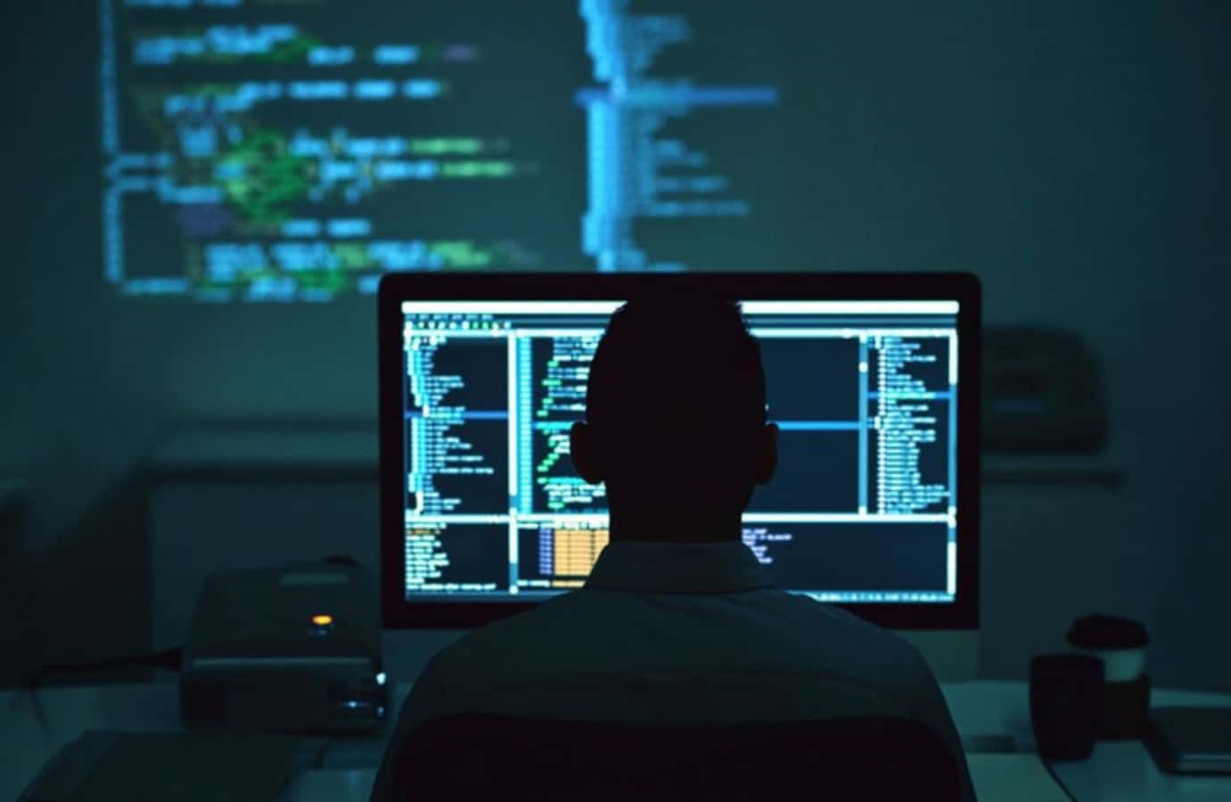 Programming 桌布 壁紙 — 一名程式設計師在發光的電腦屏幕前工作至深夜，身後牆上投射著程式碼的剪影。