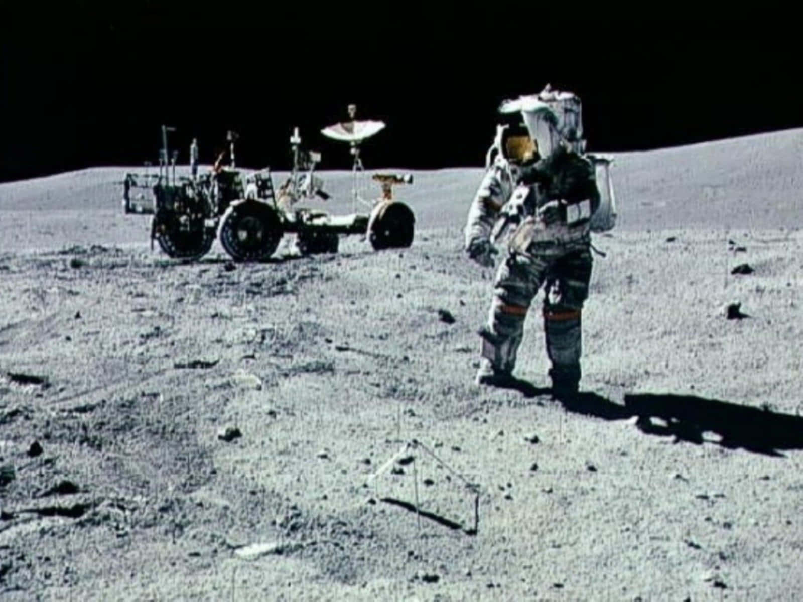 Space Mission 桌布 壁紙 — 一名穿著厚重太空衣的太空人站在月球灰色的表面上，旁邊有一輛月球車，背景是黑色的天空。