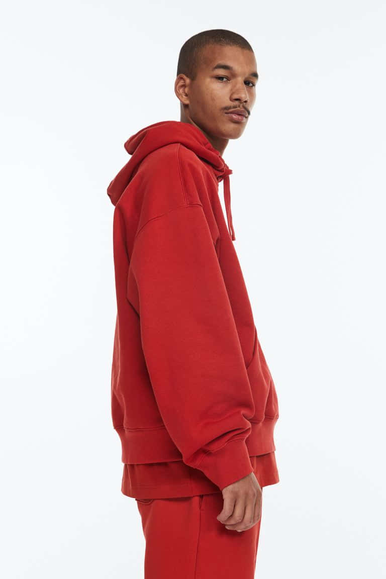 Red Hoodie 桌布 壁紙 — 一名穿著大膽紅色連帽衫和配套褲子的男子，在純白色背景下側面站立。