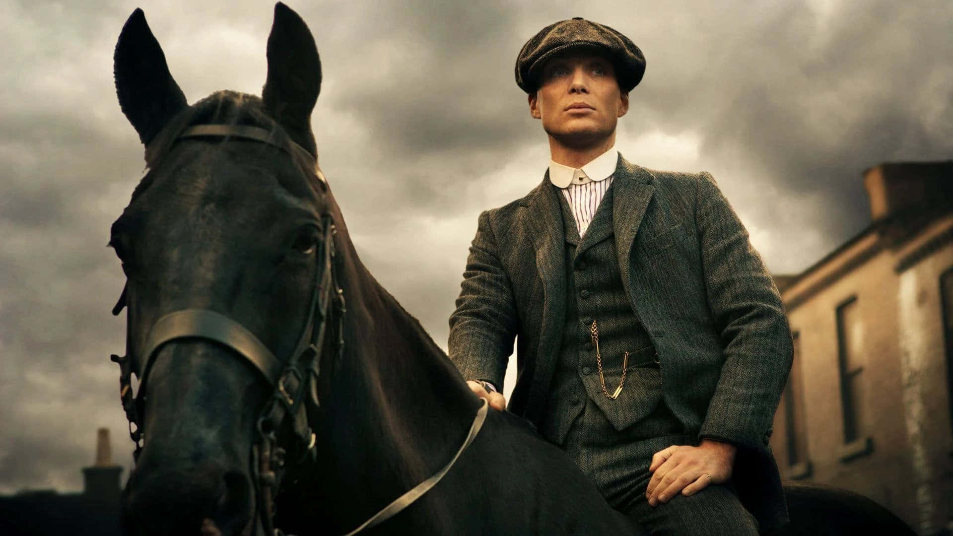 Peaky Blinders 桌布 壁紙 — 一名穿著復古西裝和扁帽的男子騎在一匹黑馬上，背景是陰沉的陰天和磚砌建築。