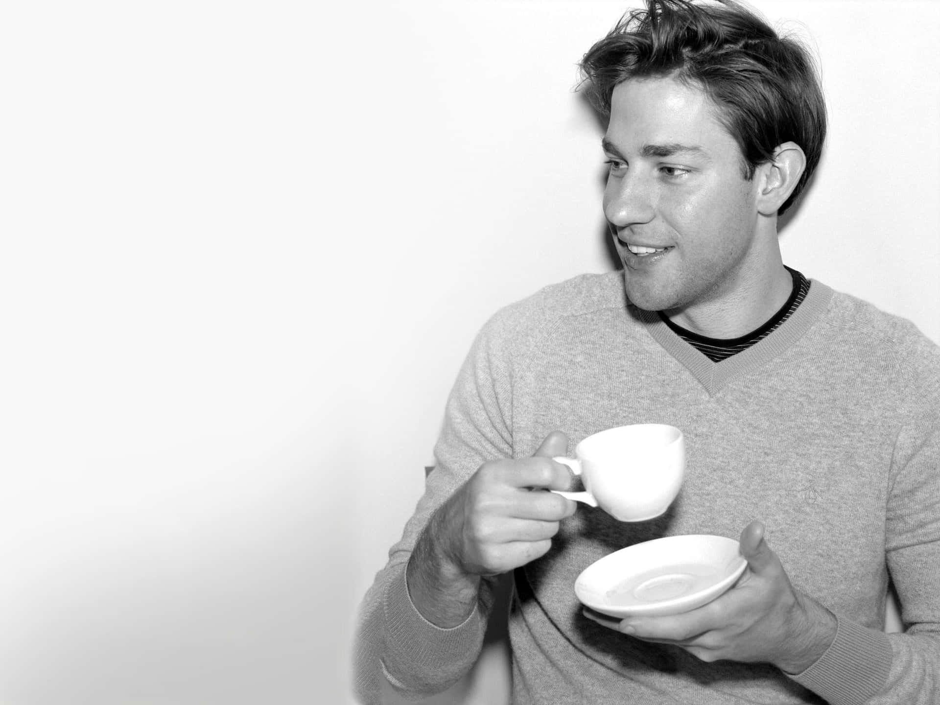 john krasinski 桌布 壁紙 — 一名穿著毛衣的男子在純白背景前微笑，手持茶杯和茶托。