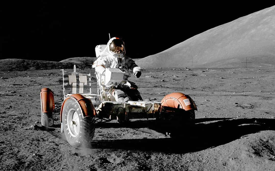 Lunar Rover 桌布 壁紙 — 一名穿著白色太空衣的太空人在黑色天空下，駕駛橙色月球車行駛在荒蕪的灰色月球表面。