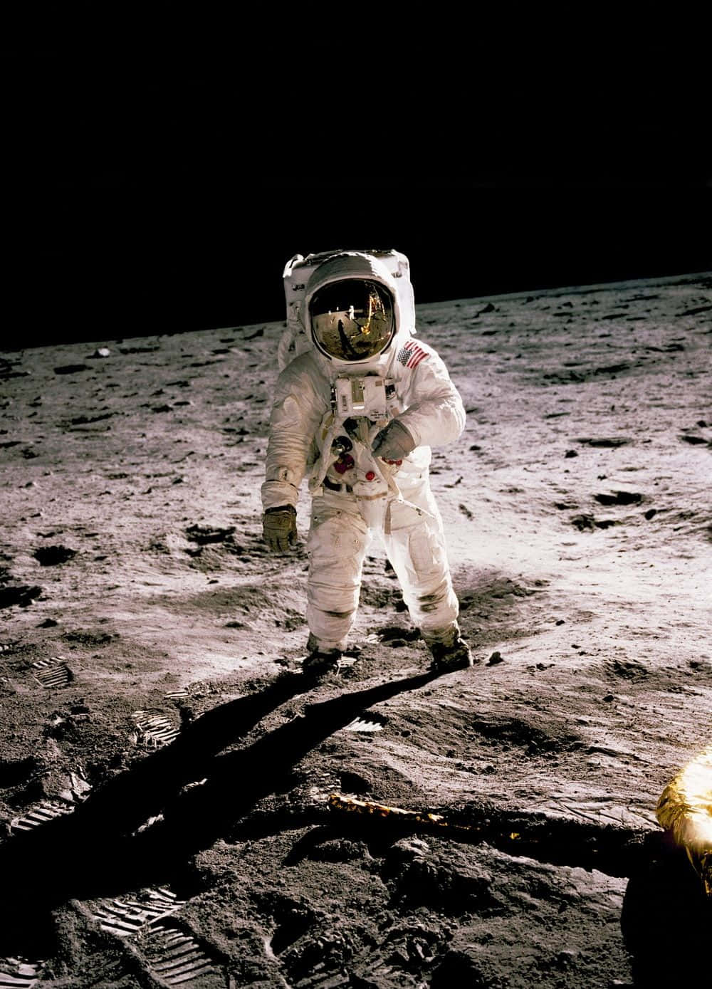 Space Mission 桌布 壁紙 — 一名穿著白色太空衣的太空人站在月球灰色的表面上，在明亮的陽光下投射出長長的影子，背後是黑色的天空。