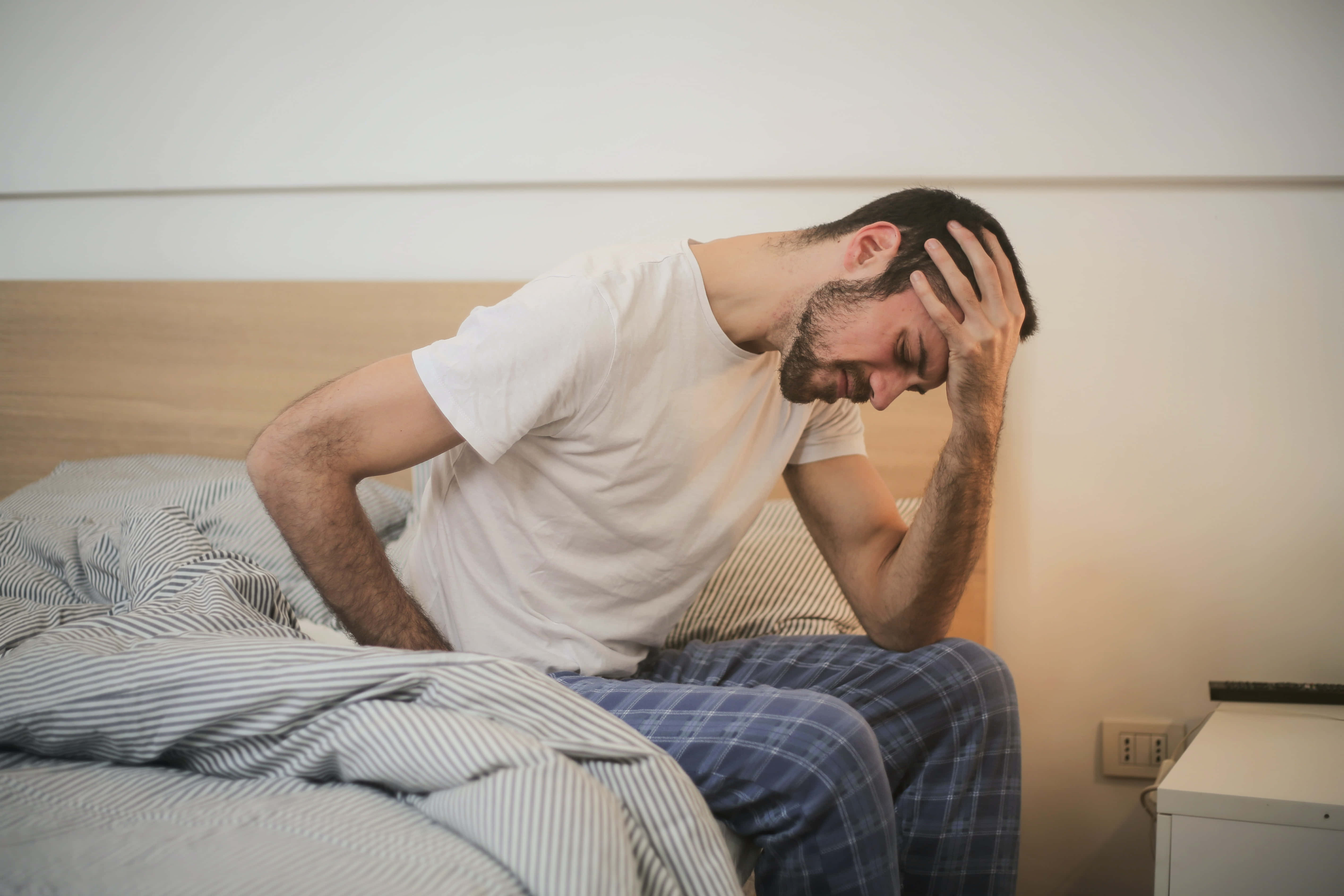 hurt 桌布 壁紙 — 一名穿著睡衣的男子坐在床上，明顯痛苦或疼痛地抱著頭。