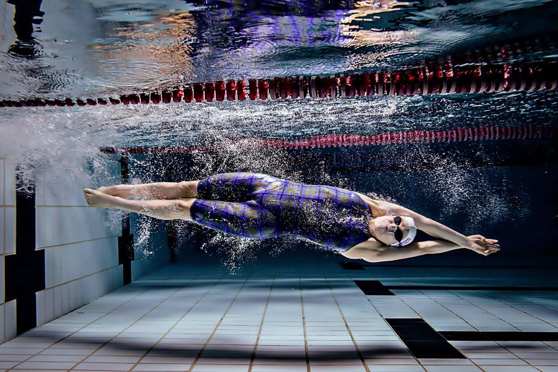 Swimming 桌布 壁紙 — 一名穿著紫色圖案泳衣的泳手在設有紅色泳線分隔和瓷磚牆的泳池中潛水滑行。