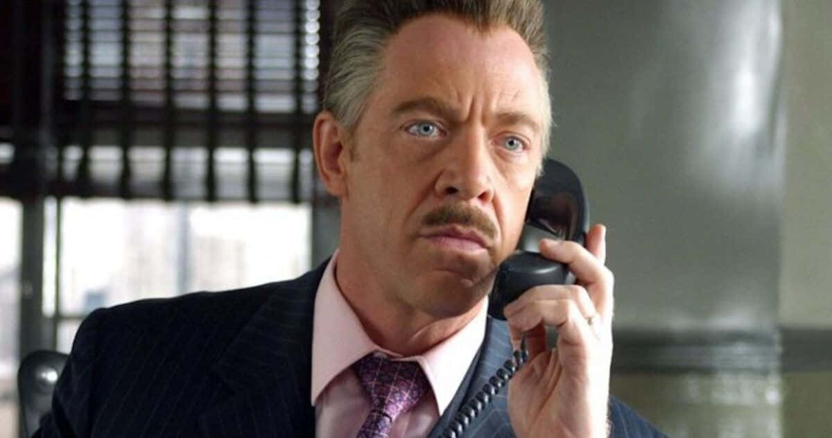 J Jonah Jameson 桌布 壁紙 — 一名穿著細條紋西裝的男子在帶有百葉窗的辦公室裡，表情嚴肅地將黑色電話貼在耳邊。