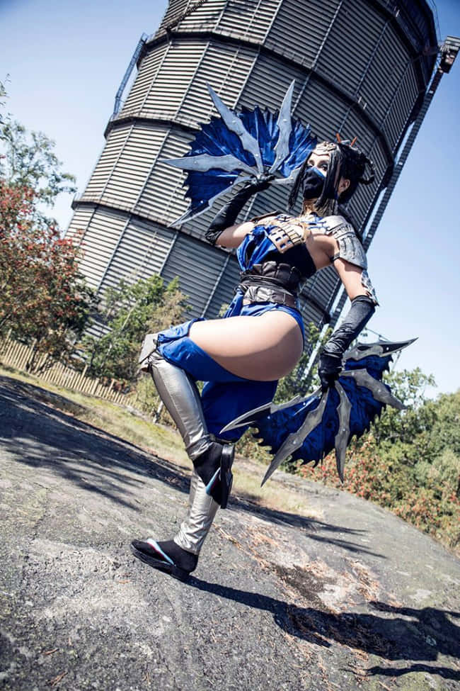 Mortal Kombat Kitana 桌布 壁紙 — 一名穿著藍銀色服裝、戴著翼狀護手的角色扮演者在大型工業水塔前擺出動感姿勢。