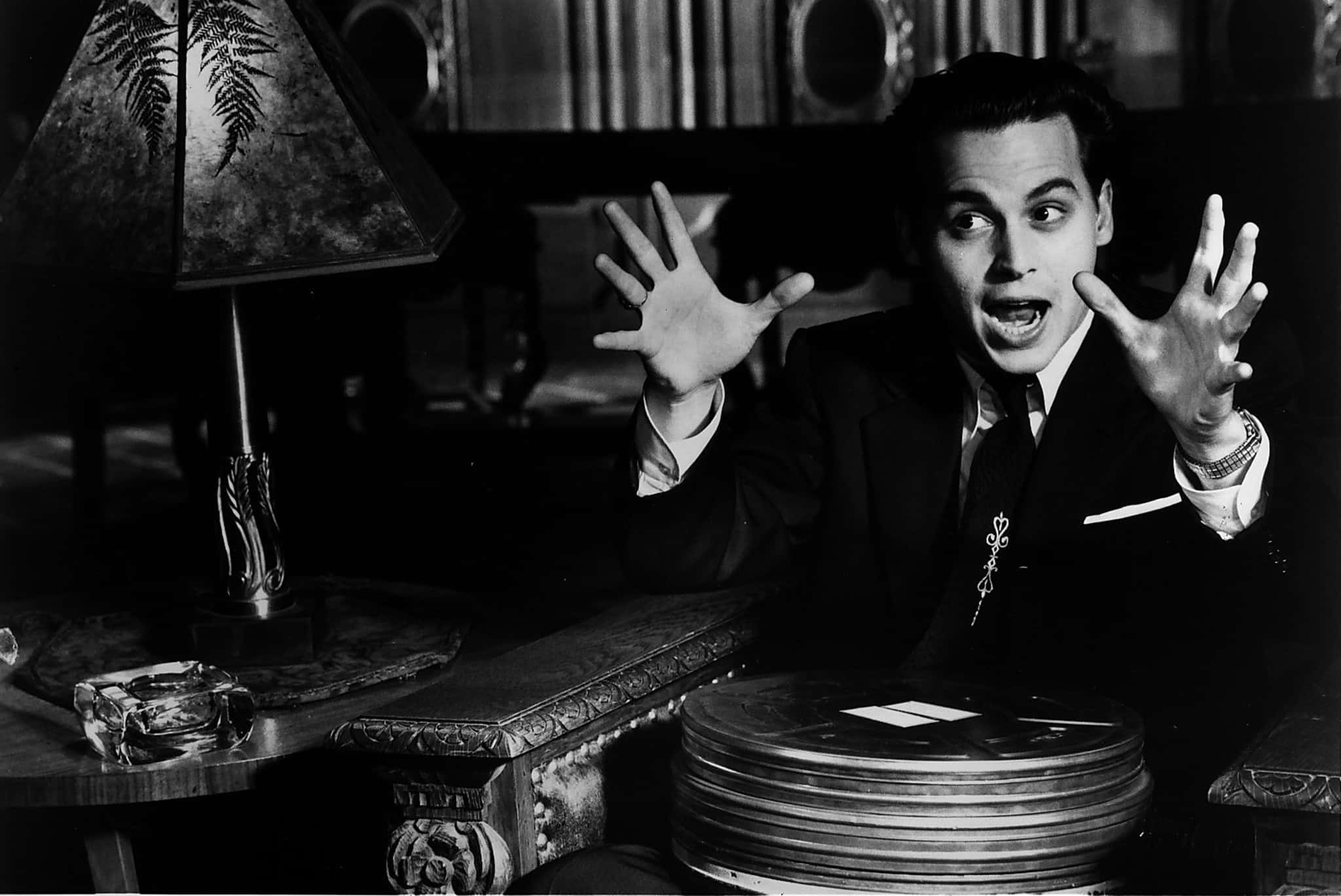 Classic Movie 桌布 壁紙 — 一名穿著西裝的男子戲劇性地坐在昏暗的復古房間裡，雙手舉起，旁邊放著一堆膠片卷。