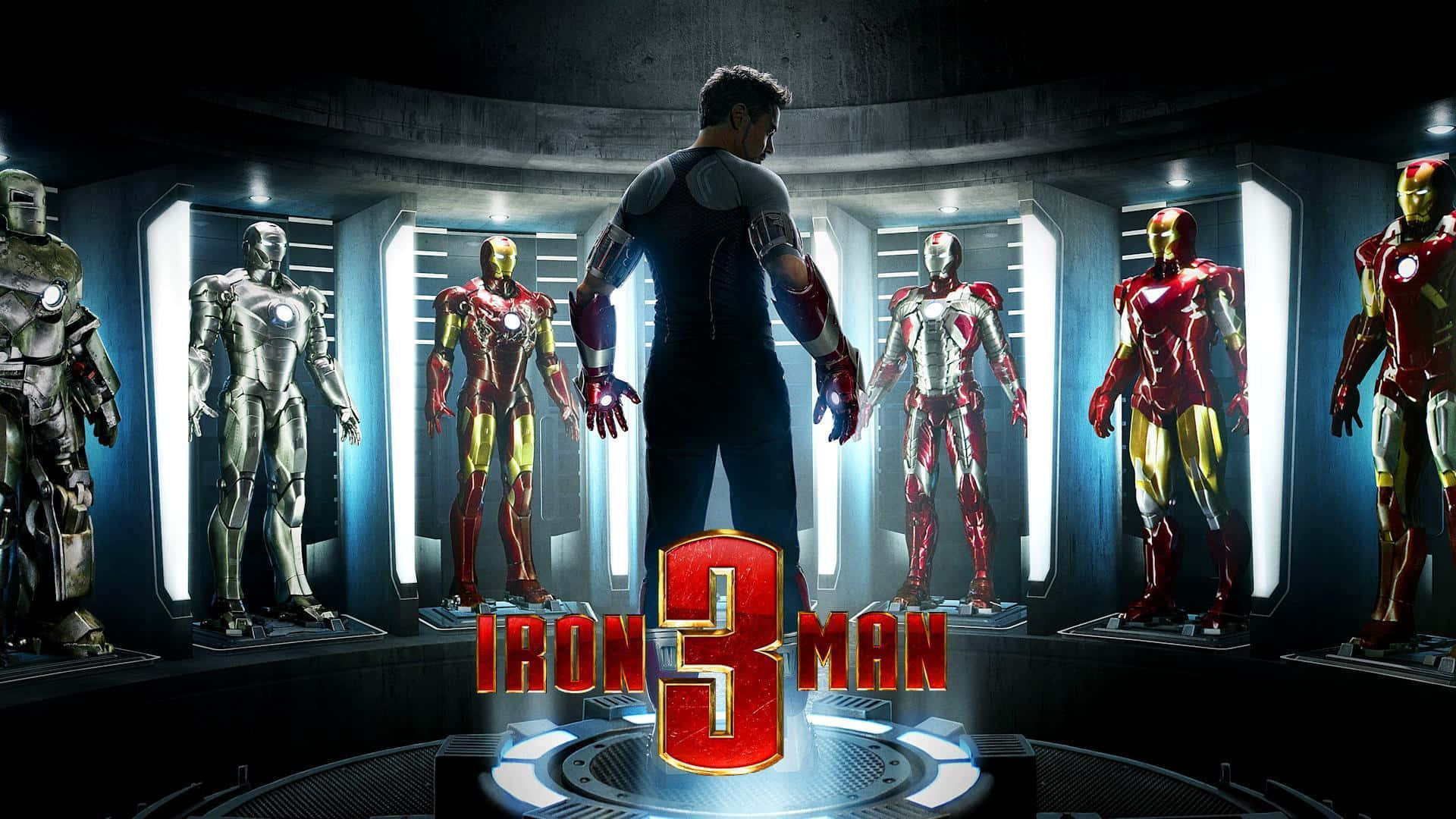 Iron Man Suit 桌布 壁紙 — 一名穿著西裝的男子站在一個高科技實驗室中，面前是圓形展示的多種鐵甲奇俠戰衣，周圍有發光的燈光。