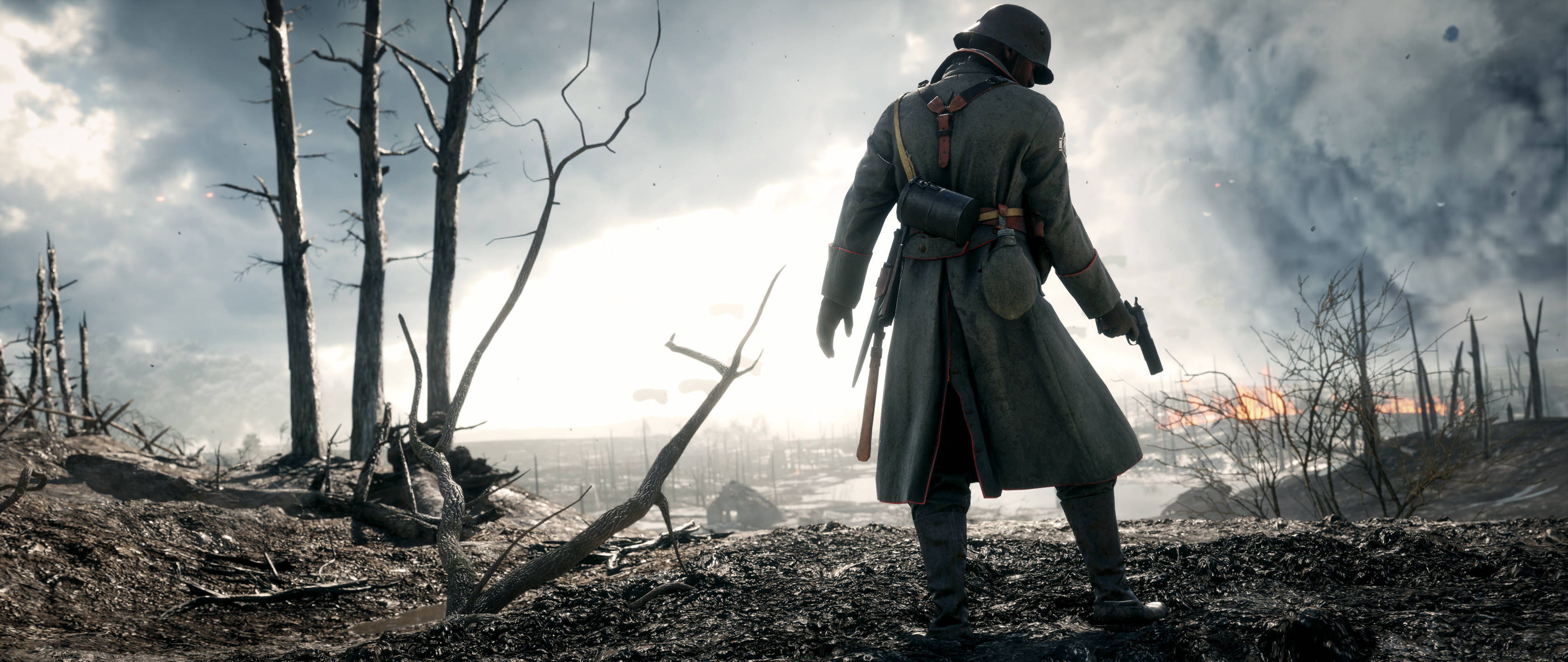 Battlefield 1 HD 桌布 壁紙 — 一名穿著風衣的士兵獨自站在荒涼的戰場上，有光禿的樹木和遠處的火災，天空多雲。
