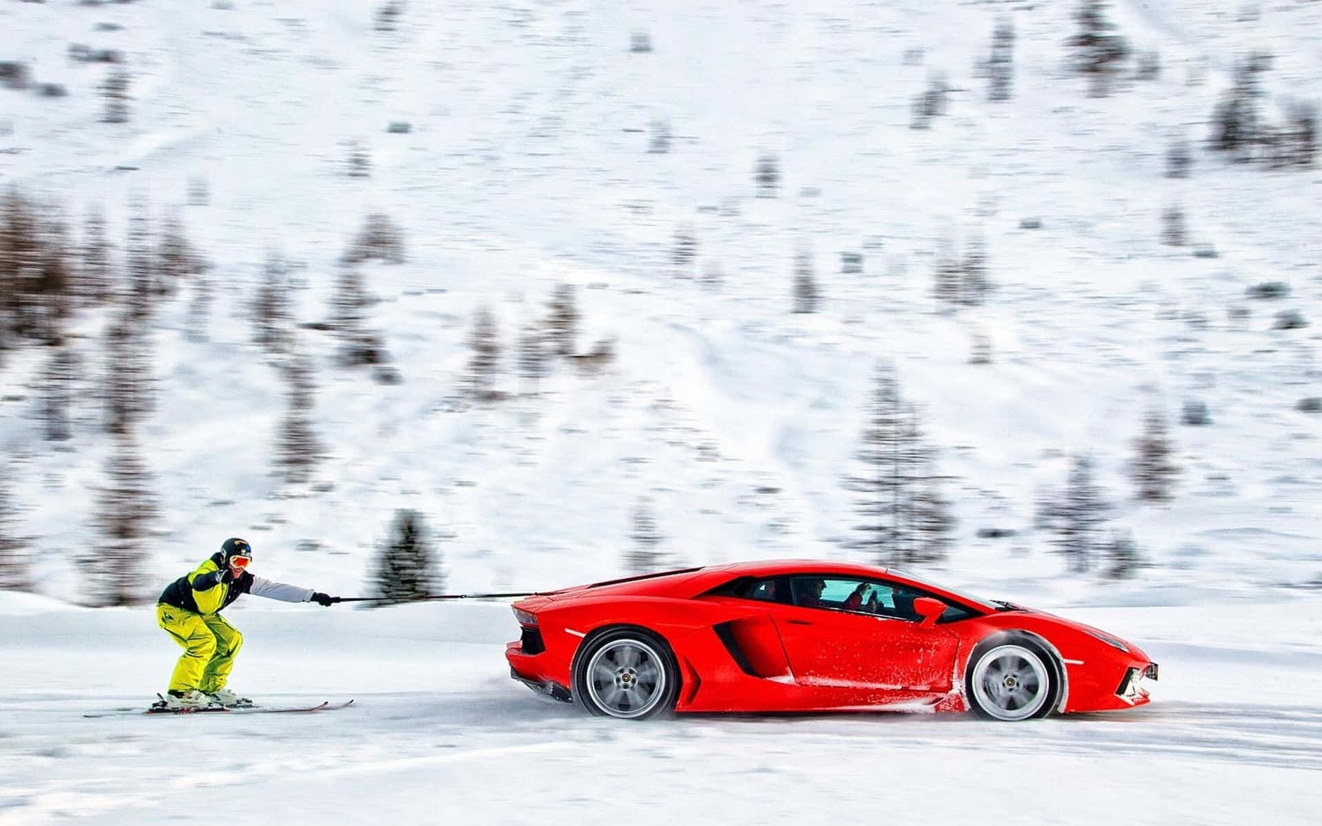 Skiing 桌布 壁紙 — 一名穿著鮮艷裝備的滑雪者，在動態模糊效果下，拉著一輛紅色林寶堅尼穿越白雪覆蓋的山坡。