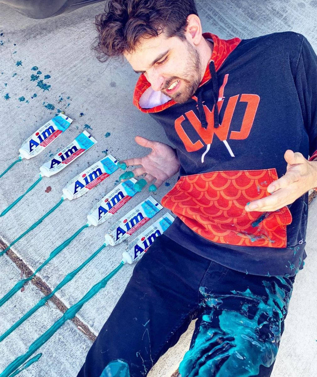 Man 桌布 壁紙 — 一名穿連帽衫的男子躺在行人路上，身上覆蓋著從多支Aim牙膏管擠出的青綠色牙膏。