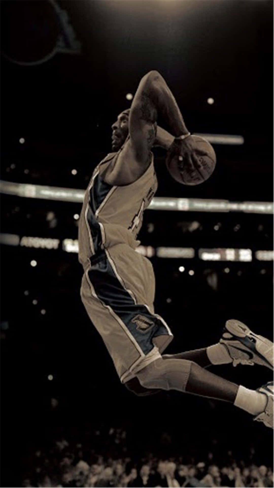 科比· Bryant 桌布 壁紙 — 一名籃球運動員在明亮的場館燈光下，於夜間比賽中進行戲劇性的灌籃，在空中翱翔。