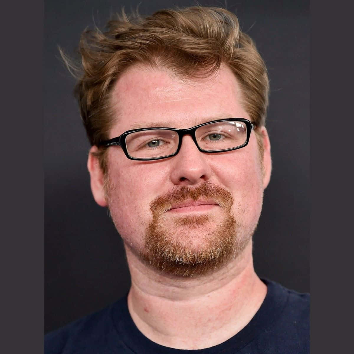 Justin Roiland 桌布 壁紙 — 一名紅棕色頭髮、戴眼鏡的男子在深灰色背景下直視鏡頭。