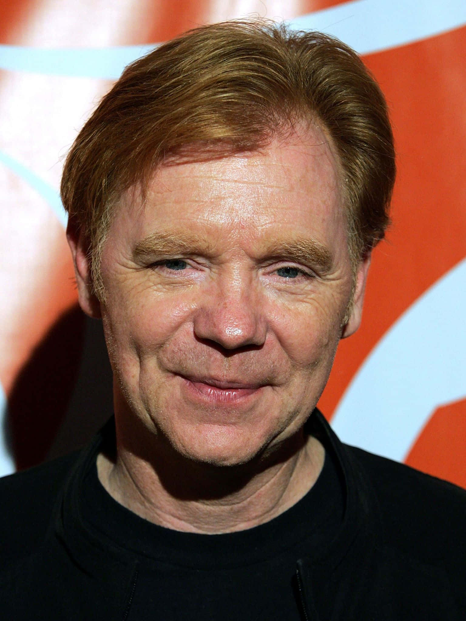 David Caruso 桌布 壁紙 — 一名紅髮藍眼男士的特寫肖像，在充滿活力的橙色和白色抽象背景前溫柔微笑。