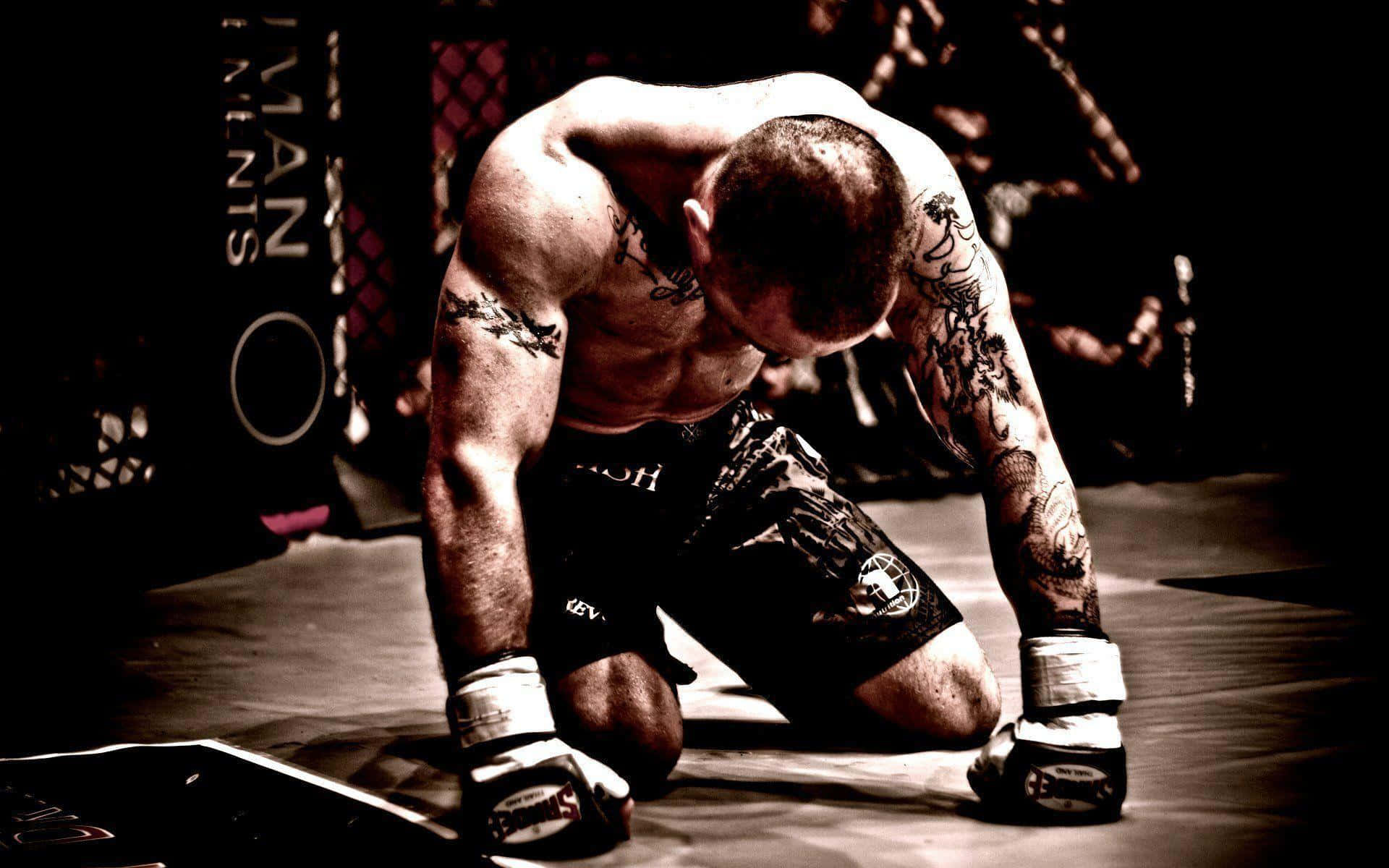 UFC 桌布 壁紙 — 一名紋身拳手在殘酷比賽後，於昏暗八角籠內的MMA墊上疲憊地跪著。