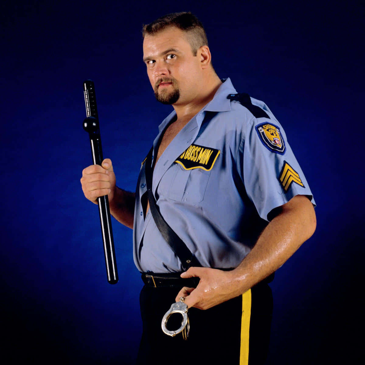 WWF Big Boss Man 壁紙 — 一名肌肉發達的男子身穿藍色警察制服，在深藍色攝影棚背景下手持警棍和手銬。