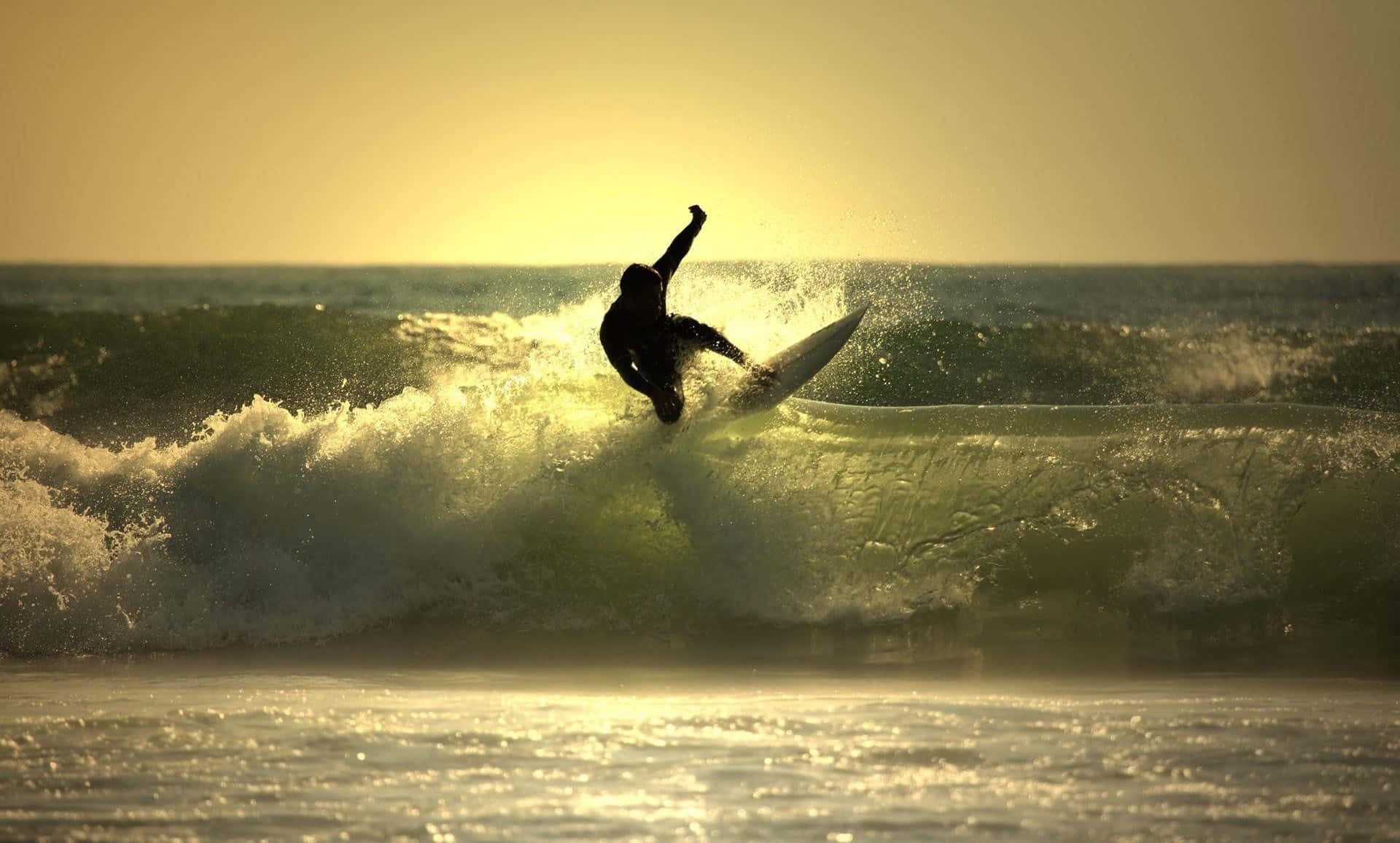 surfing 桌布 壁紙 — 一名衝浪者在日落時分乘著金色海浪，高舉雙臂，在閃耀的天空下慶祝勝利。
