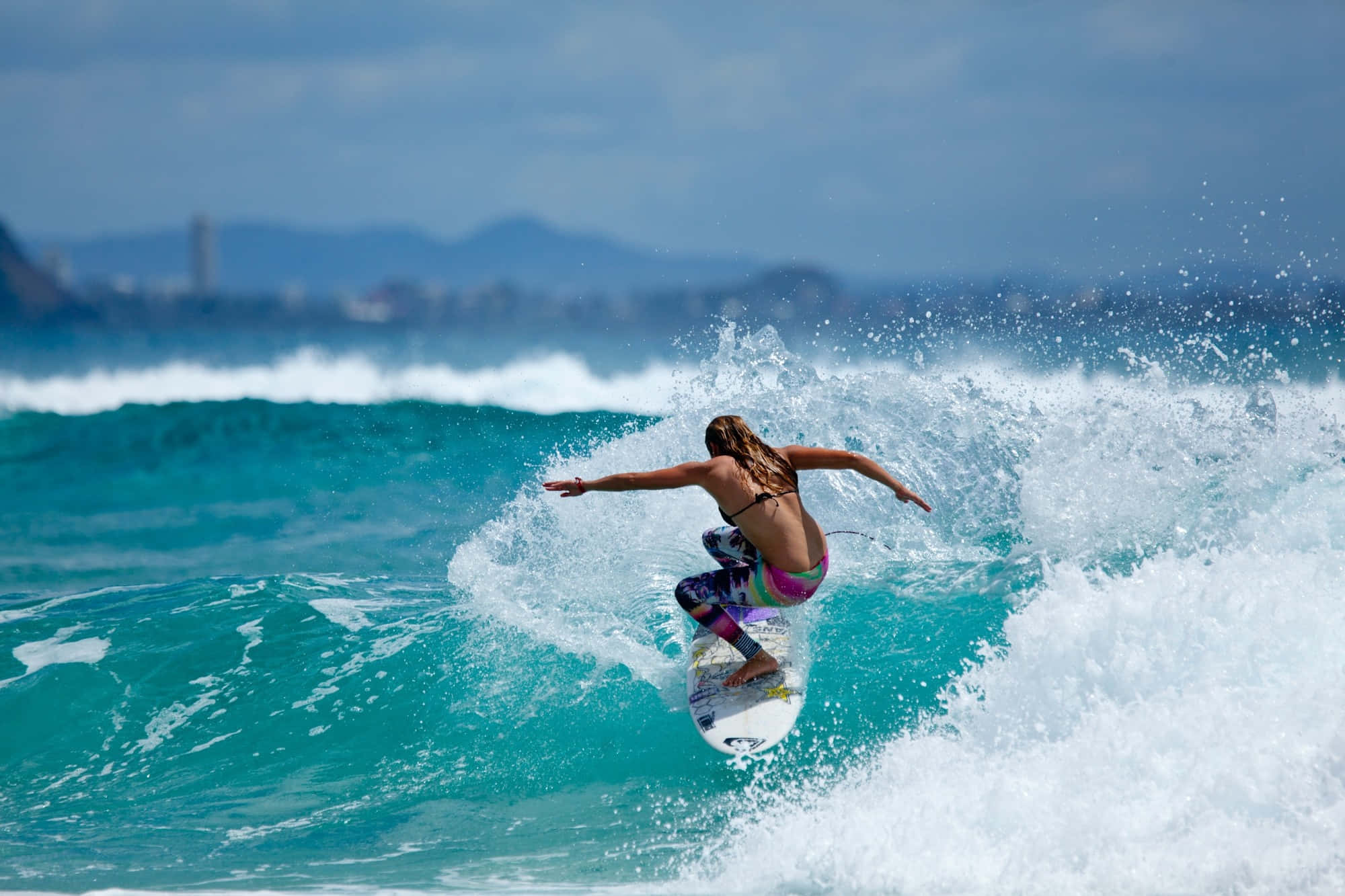 Beach Water Sports 桌布 壁紙 — 一名衝浪者在明亮的日光下，於海岸背景下張開雙臂騎乘碧綠色的海浪。