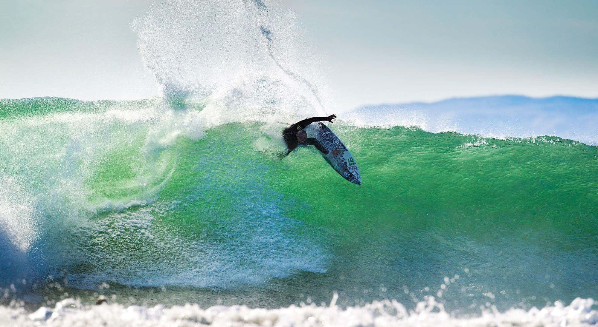 surfing 桌布 壁紙 — 一名衝浪者在明亮的日光下騎乘巨大的藍綠色海浪，周圍水花四濺。