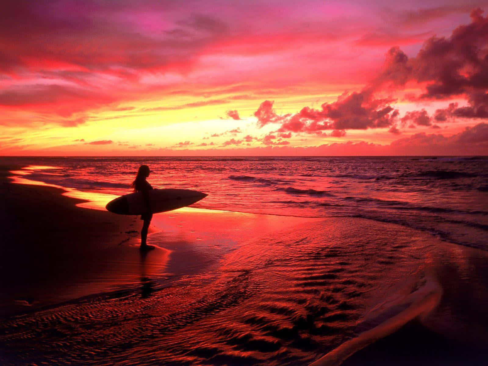 surfing 桌布 壁紙 — 一名衝浪者站在日落時分的沙灘上，呈現剪影，手持衝浪板，火紅和橙色的雲彩倒映在濕沙和海洋上。