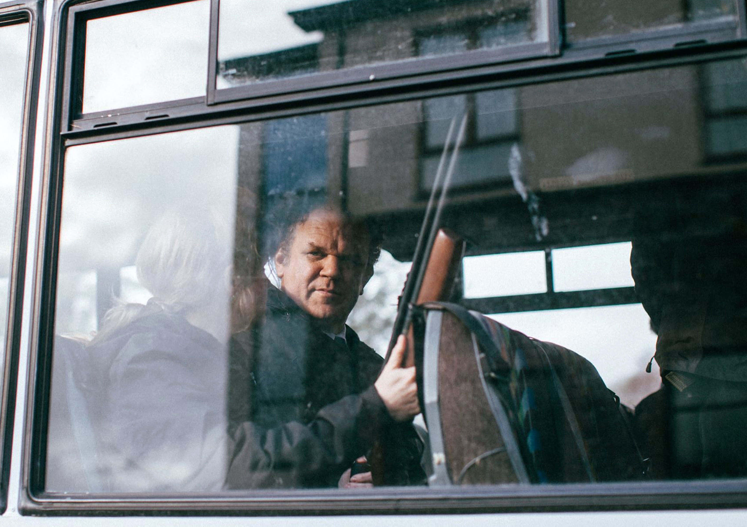 John C. Reilly 桌布 壁紙 — 一名表情嚴肅的男子在車內持步槍，透過車窗看到建築物和另一個人的倒影。
