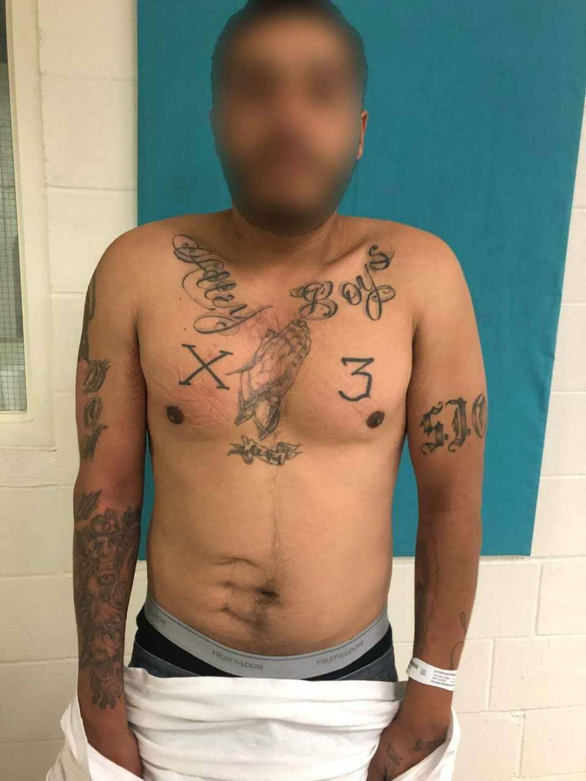 Sur 13 桌布 壁紙 — 一名赤裸上身、面容模糊的男子站在藍色牆壁前，展示包括 'Baby Boy's X 3' 和骷髏圖案在內的大量紋身。