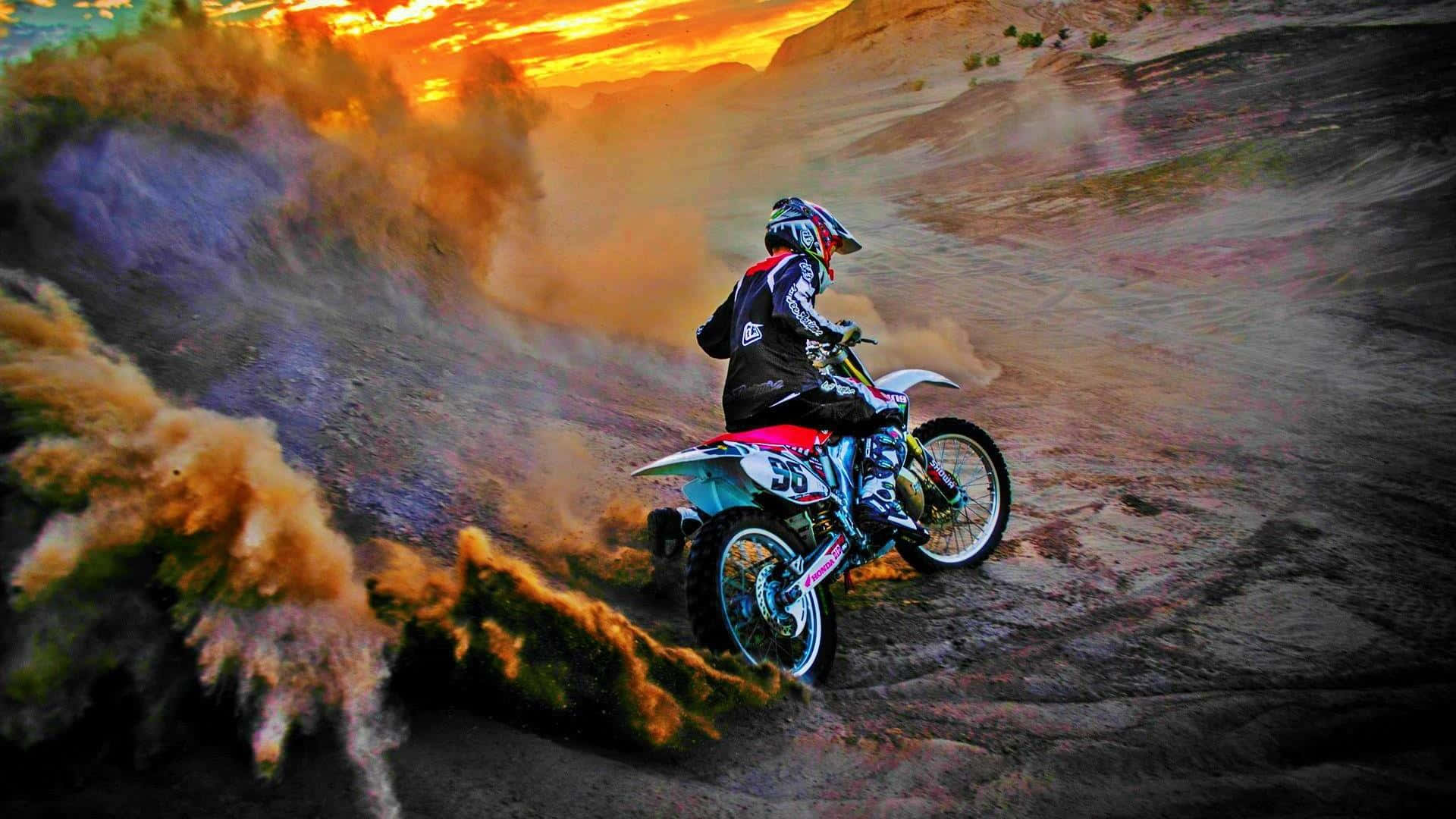 Motocross 桌布 壁紙 — 一名越野電單車手在日落時分於塵土飛揚的沙漠小徑上飛馳，揚起一大片橙色和紫色的塵雲。