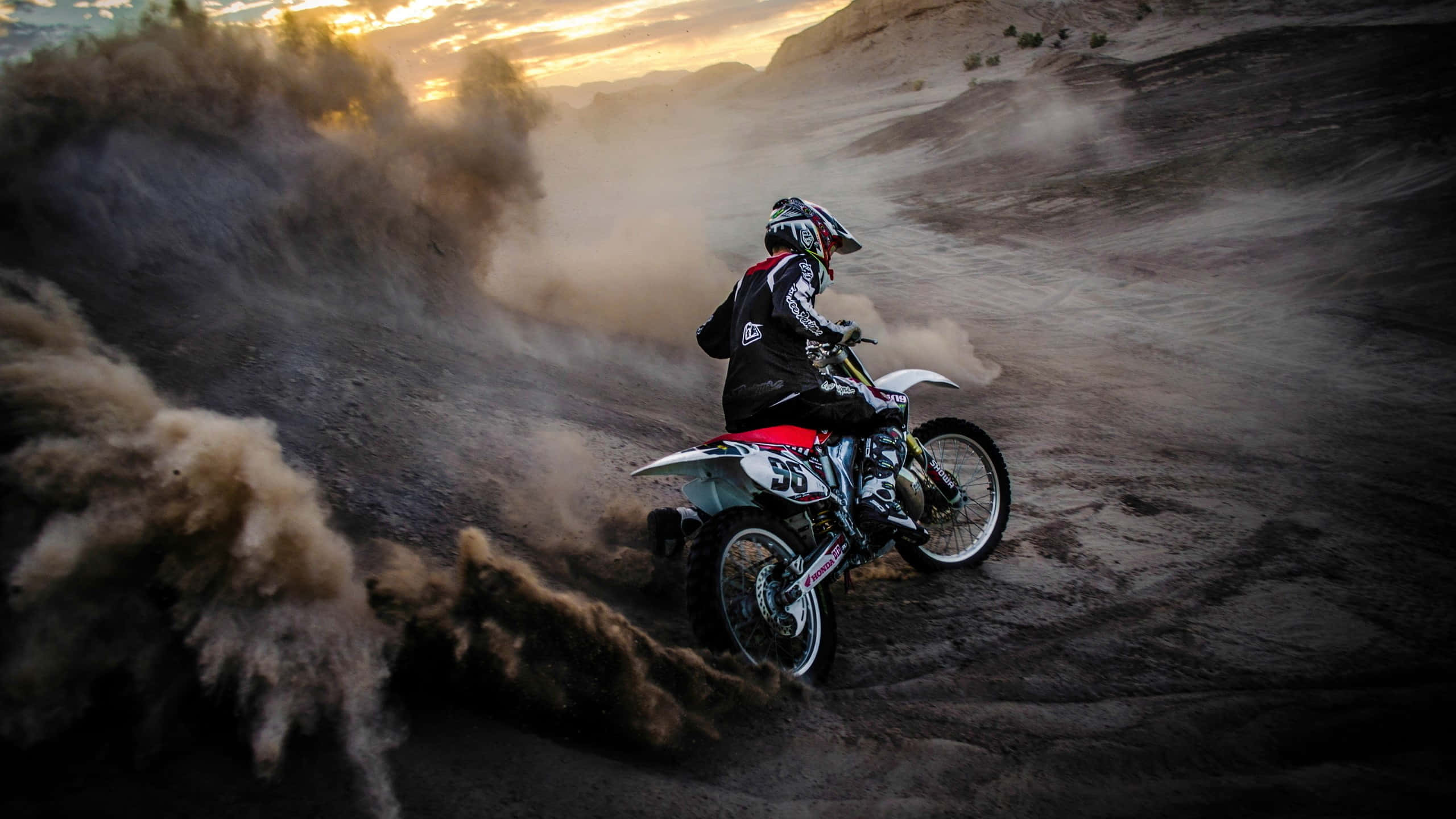Motocross 桌布 壁紙 — 一名越野電單車手在日落時分穿越塵土飛揚的沙漠峽谷，揚起巨大的沙雲。