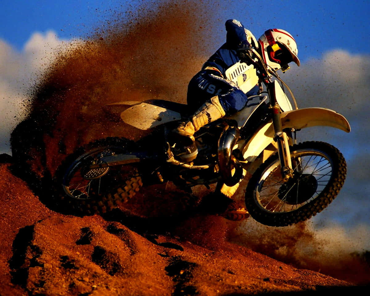 Motocross 桌布 壁紙 — 一名越野電單車手飛越泥地跳台，在藍天下揚起一大片紅褐色塵土。
